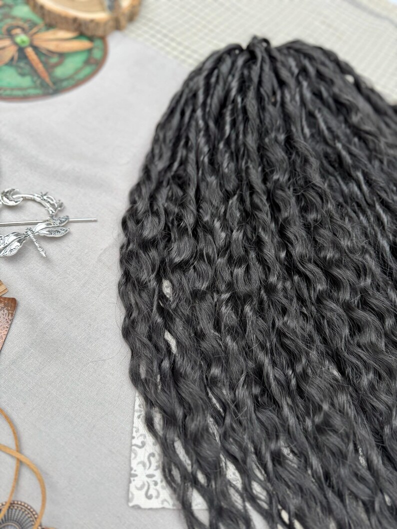 May include: A set of long, dark charcoal-colored synthetic hair extensions featuring a tight, wavy, and crimped texture. The strands are bundled together, showcasing a consistent dark tone and a wavy pattern throughout the length of the hair pieces.