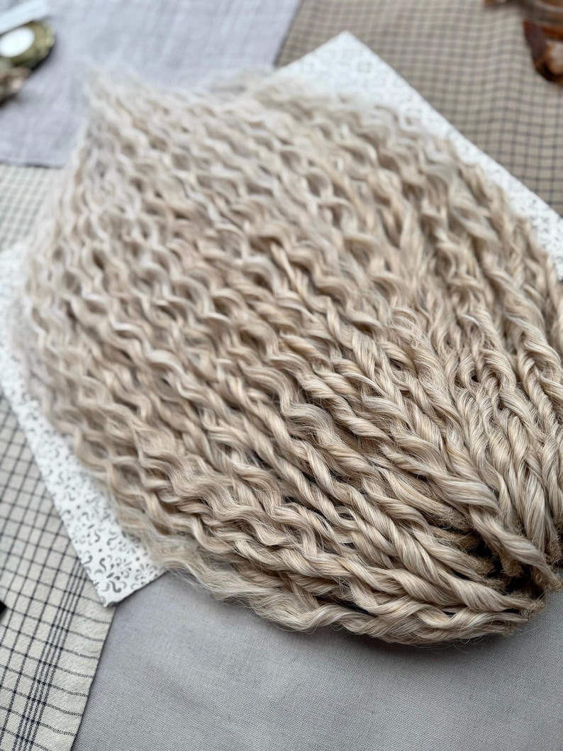 Pu&ograve; includere: Un fascio di extension per capelli biondo chiaro caratterizzato da una consistenza ondulata e crespa. Le ciocche sono disposte in un gruppo denso e uniforme, mostrando un colore beige pallido coerente lungo tutta la lunghezza delle ciocche.