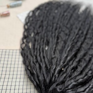 May include: A collection of long, black synthetic hair extensions styled in tight, uniform twists. The individual strands are arranged in a fan-like formation, showcasing a smooth, glossy texture and consistent thickness throughout each twisted lock.