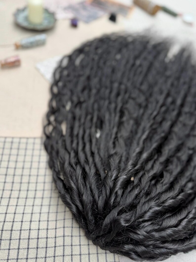 May include: A collection of long, black synthetic hair extensions styled in tight, uniform twists. The individual strands are arranged in a fan-like formation, showcasing a smooth, glossy texture and consistent thickness throughout each twisted lock.