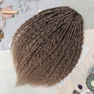 May include: A set of light brown hair extensions featuring a wavy, twisted texture. The hair is arranged in a dense, voluminous cluster with individual strands showing a consistent medium brown color throughout the length of the wavy, crimped fibers.