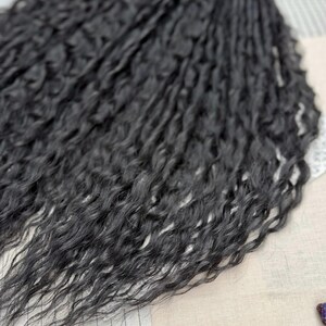 May include: A bundle of long, black hair extensions featuring a deeply wavy, crimped texture. The strands are dark, uniform in color, and arranged in a dense, flowing cluster that highlights the intricate, repetitive wave pattern throughout the length.