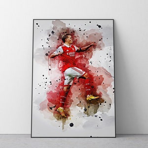 May include: A watercolor painting of a soccer player in a red and white uniform with the text "Emirates Fly Better" on the front. The player is kicking the ball with their right foot and is in mid-air. The background is a light gray with splashes of red and black paint.