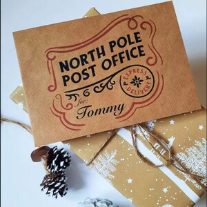 May include: A brown paper envelope with the text "North Pole Post Office" in black lettering. The envelope has a red border and a red stamp that says "Express Delivery" with a snowflake in the center. The envelope is addressed to "Tommy".