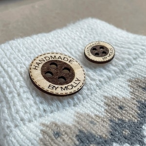May include: Two wooden buttons with the text "Handmade by Molly" on a white knitted fabric with brown and grey stripes.