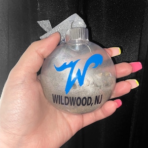 May include: A silver Christmas ornament with a blue wave design and the text "WILDWOOD, NJ".