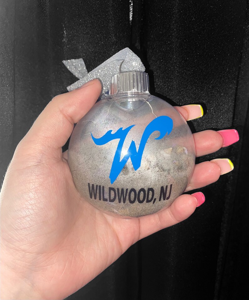 May include: A silver Christmas ornament with a blue wave design and the text "WILDWOOD, NJ".