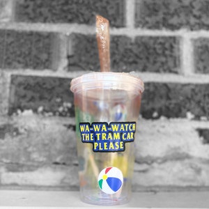 以下が含まれることがあります： ストローとビーチボールが入った透明なプラスチック製のタンブラー。タンブラーには、「WA-WA-WATCH THE TRAM CAR PLEASE」と書かれた青と黄色のステッカーが付いています。
