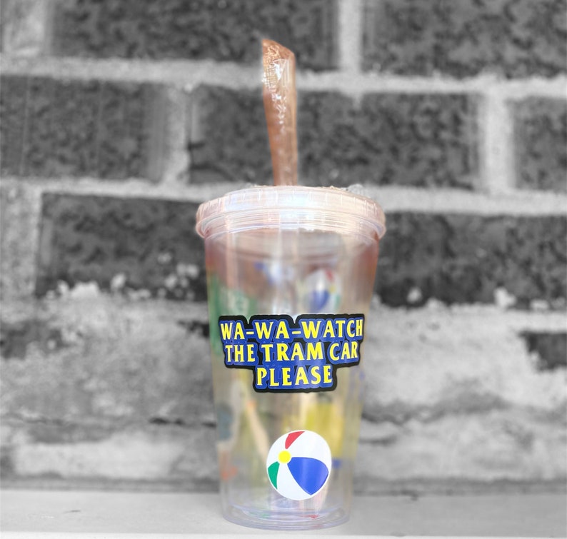 以下が含まれることがあります： ストローとビーチボールが入った透明なプラスチック製のタンブラー。タンブラーには、「WA-WA-WATCH THE TRAM CAR PLEASE」と書かれた青と黄色のステッカーが付いています。
