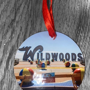 May include: A round, white ornament with a picture of the Wildwoods boardwalk. The boardwalk is closed until further notice. The image shows a sign with the text "Wildwoods Boardwalk Closed Until Further Notice". There are colorful beach balls on the boardwalk.