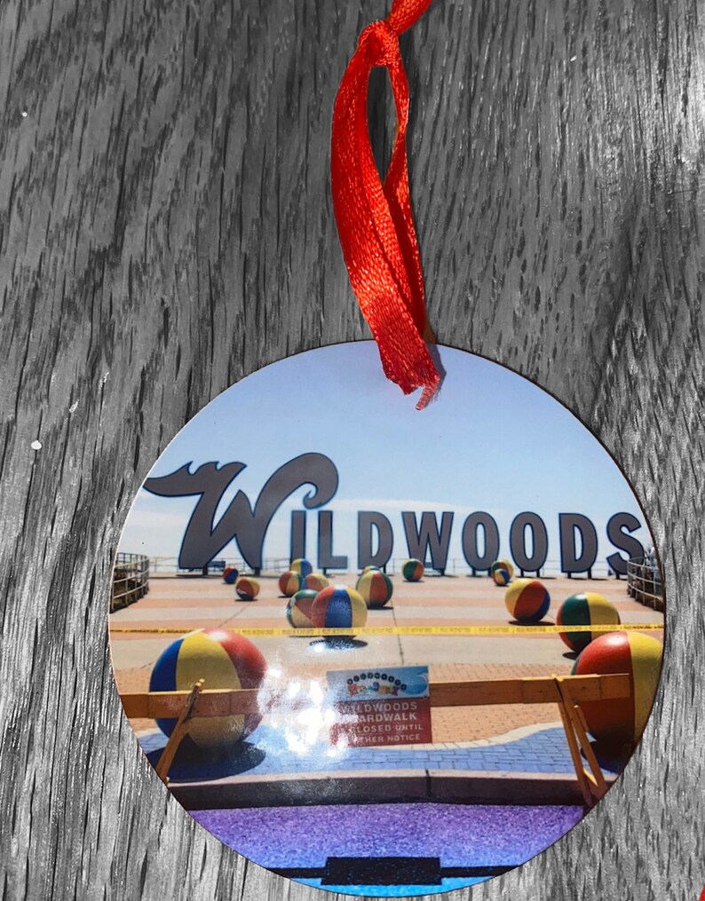 May include: A round, white ornament with a picture of the Wildwoods boardwalk. The boardwalk is closed until further notice. The image shows a sign with the text "Wildwoods Boardwalk Closed Until Further Notice". There are colorful beach balls on the boardwalk.