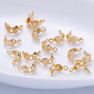 May include: A close-up of 14 gold-toned metal jewellery clasps. The clasps are designed with a curved shape and have two small loops on each side.