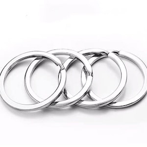 May include: Four silver key rings in a row. The rings are circular with a smooth, reflective surface. The key rings are made of metal and are suitable for organizing keys.