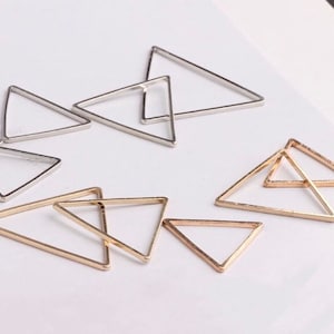 May include: A set of gold and silver triangle shaped metal hoops. The hoops are of varying sizes and are arranged in a random pattern.