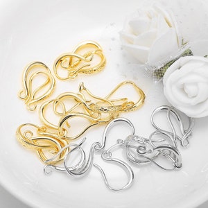 May include: A close-up of a group of gold and silver earring hooks. The hooks are made of metal and have a textured finish. They are arranged in a pile on a white surface.