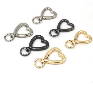 May include: Five heart-shaped metal keyrings in silver, black, and gold. Each keyring has a swiveling ring and a spring-loaded clasp.