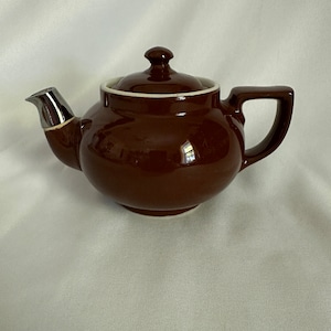 May include: A brown ceramic teapot with a silver spout and lid. The teapot has a rounded body and a simple design.
