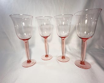 May include: Set of four pink glass wine glasses with a delicate tulip shape. The glasses have a clear body and a pink stem and base.