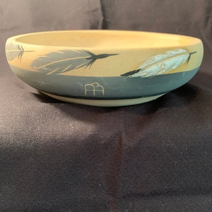 May include: A large, cream-colored ceramic bowl with a dark gray band around the rim. The bowl is decorated with a design of gray and white feathers.