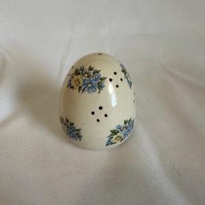 May include: White ceramic egg-shaped container with blue and yellow floral design and holes for ventilation.