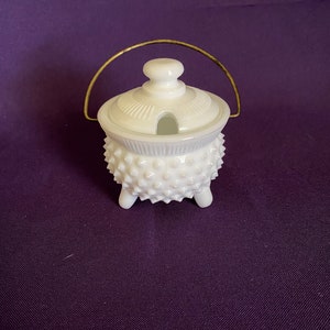 May include: White milk glass sugar bowl with a gold handle and a lid with a small spout. The bowl has a textured, spiky design.