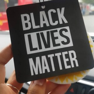May include: Black and white car air freshener with the text "Black Lives Matter" in white letters on a black background.