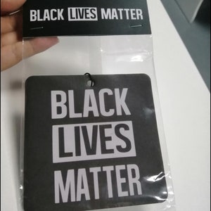 May include: Black car air freshener with the text "Black Lives Matter" in white letters on a black background.