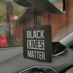 May include: Black car air freshener with the text "Black Lives Matter" in white letters on a black background.