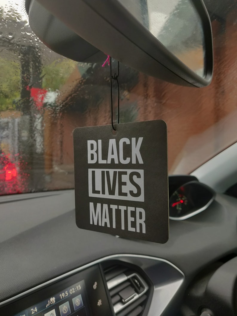 May include: Black car air freshener with the text "Black Lives Matter" in white letters on a black background.