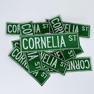 May include: A pile of green fabric patches with white text that reads "Cornelia St." The patches are in various sizes and orientations.