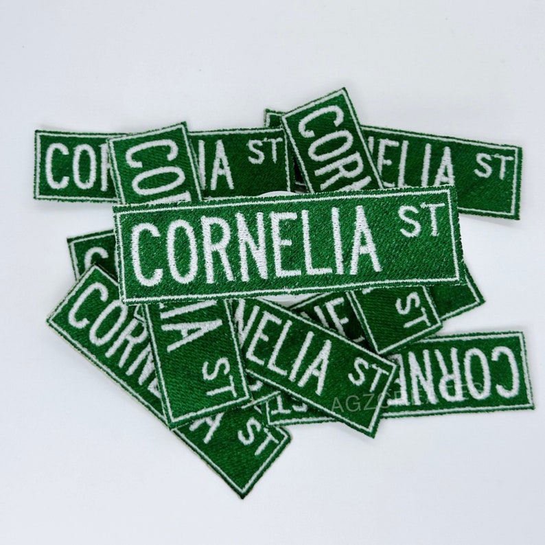 K&ouml;nnte beinhalten: Ein Stapel gr&uuml;ner Stoff-Patches mit wei&szlig;em Text, der "Cornelia St." lautet. Die Patches sind in verschiedenen Gr&ouml;&szlig;en und Ausrichtungen.
