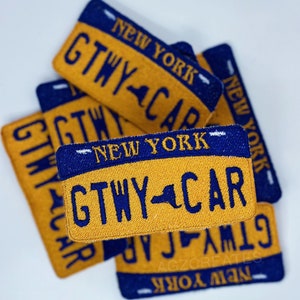 K&ouml;nnte beinhalten: Ein Stapel von vier gestickten Patches in Gelb und Blau mit dem Text "NEW YORK" und "GTWY CAR". Die Patches haben die Form eines Nummernschilds.
