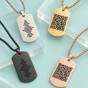 Peut inclure: Quatre pendentifs de type plaque militaire sur chaînes à maillons carrés, déclinés en argent, or, noir et or rose. Deux pendentifs présentent une onde sonore gravée en noir, tandis que les deux autres affichent un QR code gravé en noir.