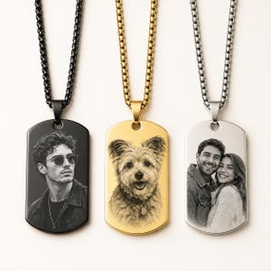 May include: Three rectangular dog tag pendants on matching box chains. The left is black with a portrait of a person wearing sunglasses. The centre is gold with a portrait of a dog. The right is silver with a portrait of a couple smiling together.