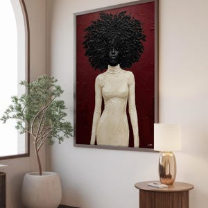 May include: A framed portrait features a woman with a large, textured black afro. She wears a cream-colored, long-sleeved dress with a high neckline. The background is a deep red, and the artwork is displayed in a room with a neutral color palette.
