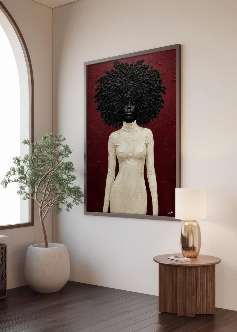 May include: A framed portrait features a woman with a large, textured black afro. She wears a cream-colored, long-sleeved dress with a high neckline. The background is a deep red, and the artwork is displayed in a room with a neutral color palette.