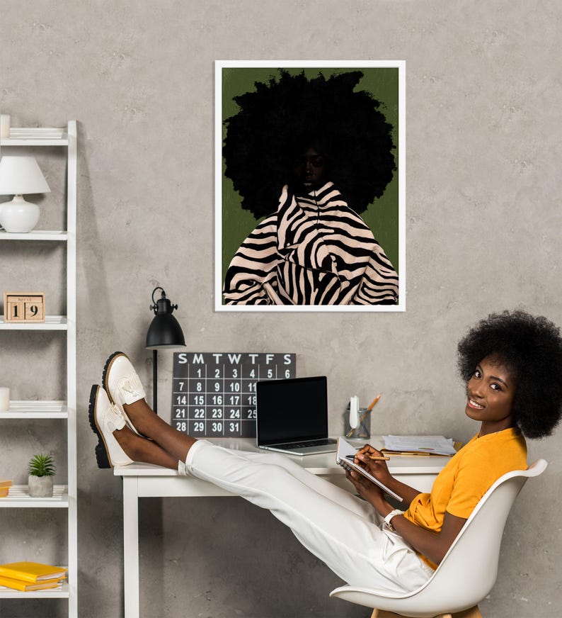 Op de afbeelding: Een ingelijste kunstdruk met een portret van een persoon met een grote afro en kleding met zebraprint. De print hangt boven een bureau met een kalender, een laptop en een persoon die op een stoel zit.