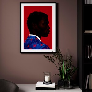 May include: Framed art print featuring a profile of a person with dark skin against a red background. The person wears a blue jacket with red accents. The artwork is displayed on a brown wall, with a candle and plant in front.