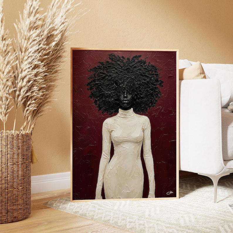 May include: A framed painting of a Black person with a large, textured afro. The figure wears a long-sleeved, off-white turtleneck dress against a deep red background. The artwork is displayed in a room with neutral tones.