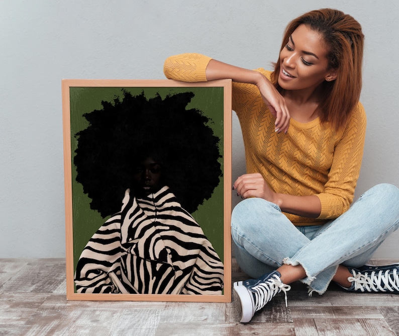 Op de afbeelding: Een ingelijste kunstdruk met een portret van een persoon met een grote, donkere afro. De persoon draagt een zwart-wit gestreept zebra-kledingstuk tegen een groene achtergrond. De lijst is lichtbruin.