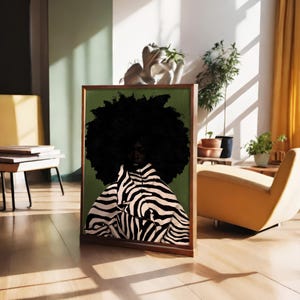 Op de afbeelding: Een ingelijste kunstdruk met een persoon met een grote, donkere afro en kleding met zebraprint tegen een groene achtergrond. Het kunstwerk wordt tentoongesteld in een lichte kamer met een houten vloer, een gele stoel en planten.