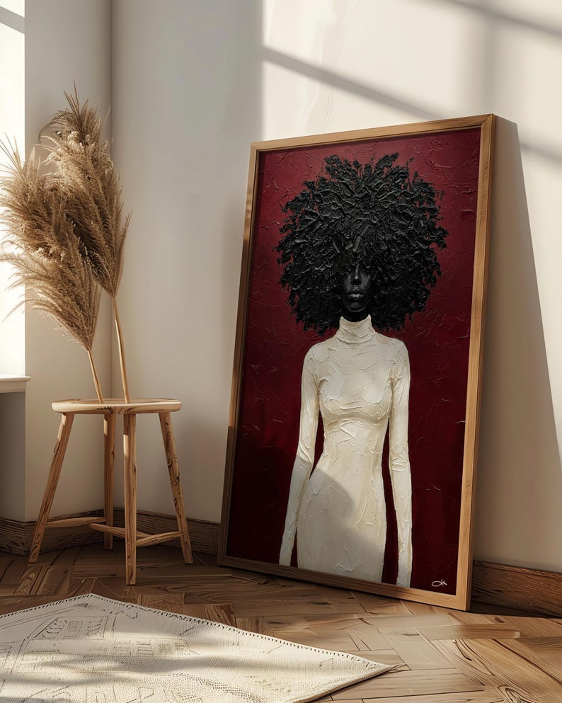 May include: A framed artwork featuring a woman with a large, textured black afro and a white turtleneck dress against a deep red background. The artwork is in a wooden frame and leans against a wall.