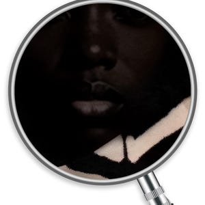 Op de afbeelding: Een close-up van een gezicht, deels in de schaduw. De focus ligt op de lippen en neus. Een zwart-wit patroonstof is zichtbaar in de rechter benedenhoek, wat een textuurcontrast aan de afbeelding toevoegt.