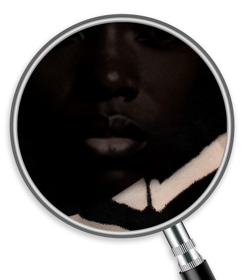 Op de afbeelding: Een close-up van een gezicht, deels in de schaduw. De focus ligt op de lippen en neus. Een zwart-wit patroonstof is zichtbaar in de rechter benedenhoek, wat een textuurcontrast aan de afbeelding toevoegt.