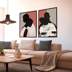 May include: Two framed wall art prints featuring silhouettes of people. The left print shows two figures in profile against a pink and grey background. The right print depicts two figures embracing, one wearing a blue and white patterned shirt.