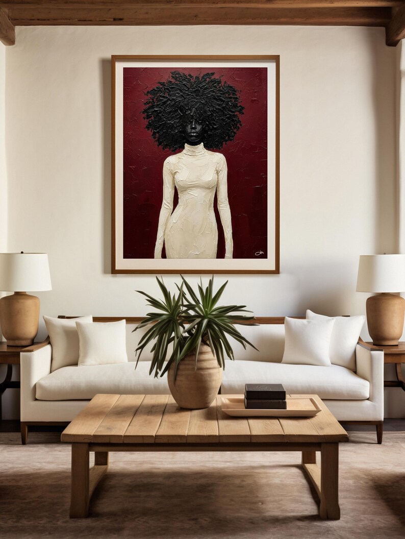 May include: A framed artwork depicts a woman with a large, textured black afro and a white turtleneck dress against a deep red background. The artwork hangs above a white sofa with white pillows, a wooden coffee table, and two lamps.