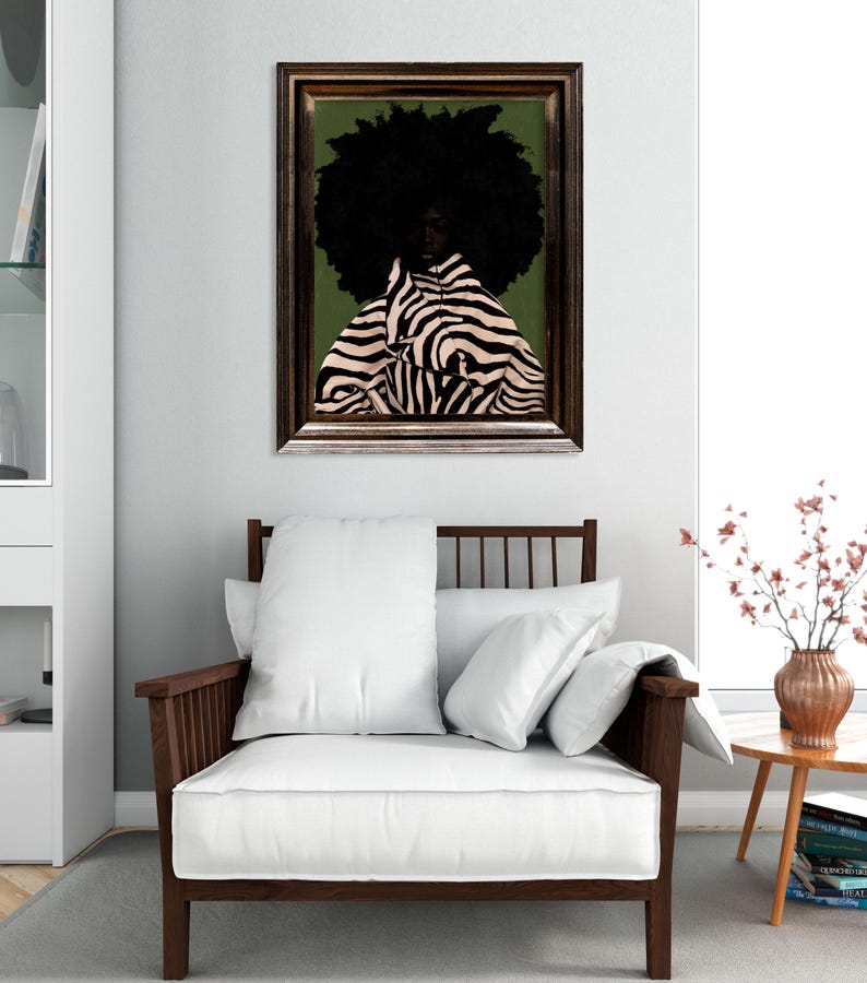 Op de afbeelding: Een ingelijst kunstwerk toont een persoon met een grote zwarte afro en een zebra-gestreept kledingstuk tegen een groene achtergrond. Het kunstwerk hangt boven een houten fauteuil met witte kussens. Een kleine bijzettafel met een vaas bloemen staat naast de stoel.
