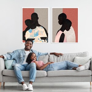 May include: Two framed wall art prints featuring black silhouettes of figures against a background of muted red and beige. The left print shows a figure carrying another, while the right print depicts two figures in profile, all with textured patterns.