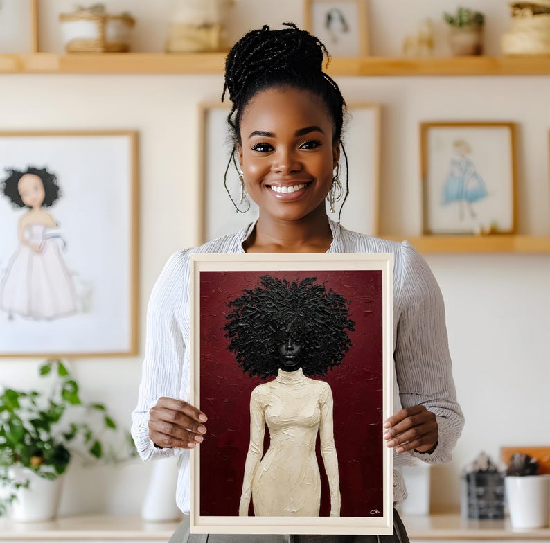 May include: A framed artwork featuring a portrait of a Black woman with a large, textured afro. She is depicted wearing a cream-colored turtleneck dress against a deep red background. The artwork is held by a smiling person.