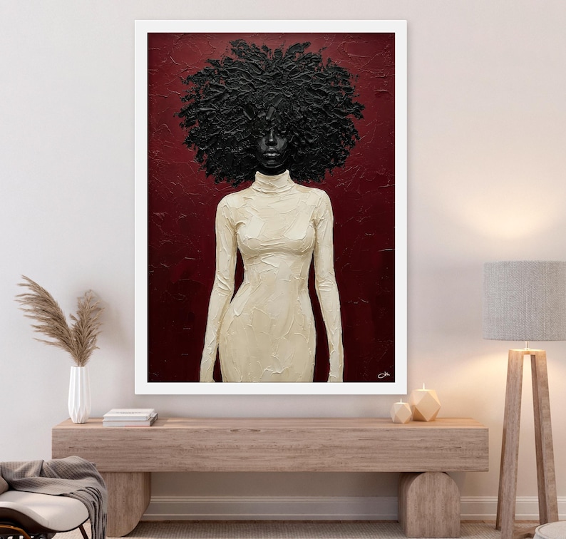 May include: A framed art print featuring a woman with a large, textured afro and a cream-colored, long-sleeved dress. The background is a deep red, and the artwork is displayed in a white frame, creating a striking contrast.